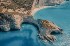 Aerial view of blue sea, mountains, white sandy beach at sunrise in summer. Porto Katsiki, Lefkada island, Greece. Beautiful landscape with sea coast, yacht, rocks, azure water, green forest. Top view